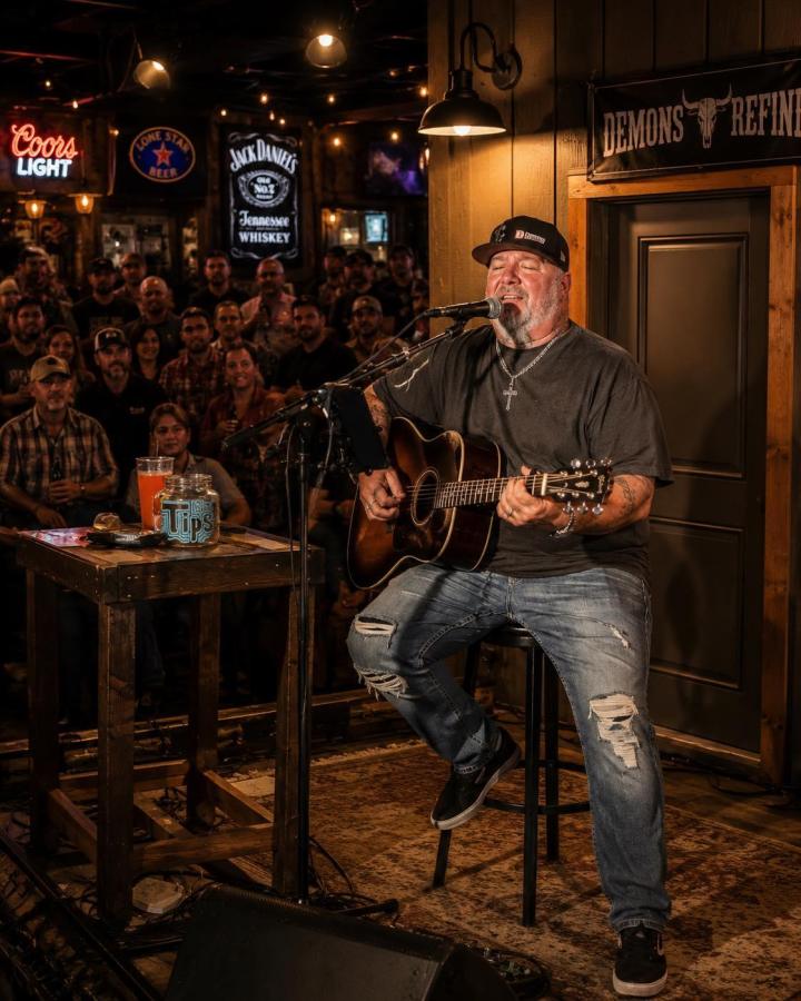 Mike Outlaw Clasey singing and playing acoustic guitar on stage for a packed country bar crowd
